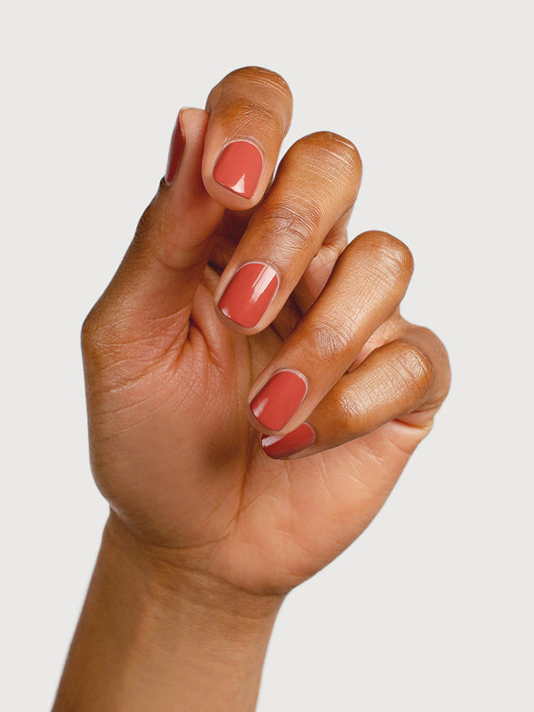 A medium-brown hand with fingers loosely curled to display glossy terracotta-red nails painted in Sienna Byron Bay Life.