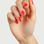 Close-up of a hand wearing Sienna Byron Bay Kiss nail polish in a vivid coral-red shade.