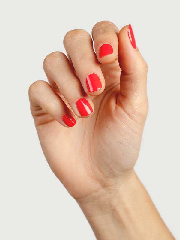 Close-up of a hand wearing Sienna Byron Bay Kiss nail polish in a vivid coral-red shade.