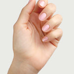A hand with neatly manicured nails painted in Sienna Byron Bay Nail Polish - Magic, a soft, pale cherry blossom pink shade, is held up against a plain light background.