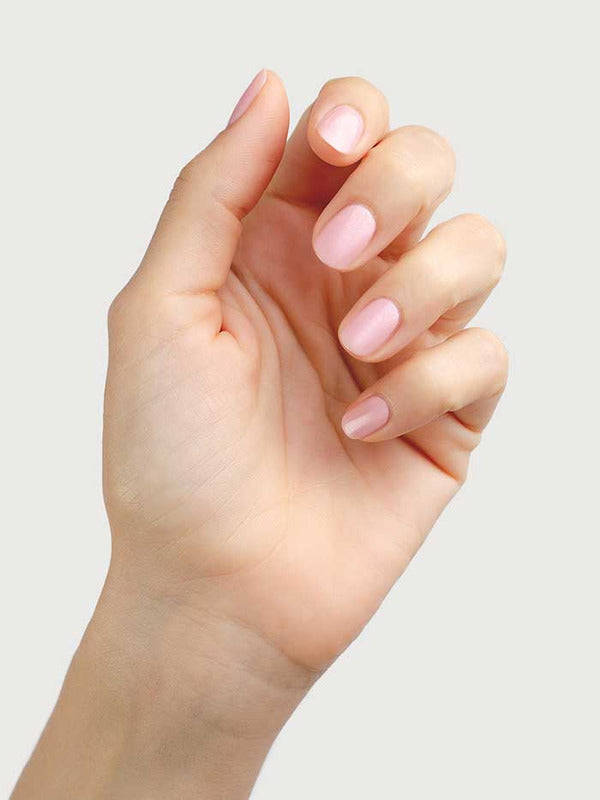 A hand with neatly manicured nails painted in Sienna Byron Bay Nail Polish - Magic, a soft, pale cherry blossom pink shade, is held up against a plain light background.