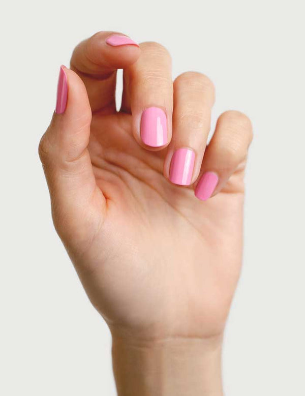 A hand with neatly manicured nails painted in Sienna Byron Bay Nail Polish - Magnolia, a glossy, plant-derived pink shade, shown against a plain light background.