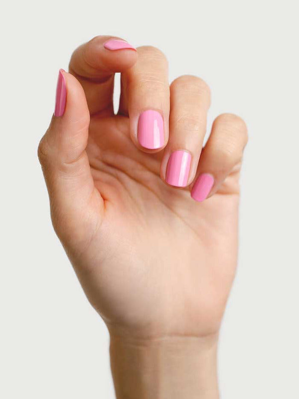 A hand with neatly manicured nails painted in Sienna Byron Bay Nail Polish - Magnolia, a glossy, plant-derived pink shade, shown against a plain light background.