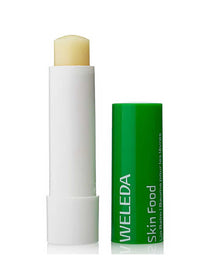 A Weleda Skin Food Lip Stick 4.8g, nourishing for dry, chapped lips, stands upright with the green cap off beside it, exposing the yellow balm inside its white tube.