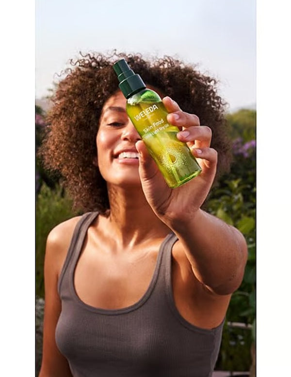Woman holding Weleda Skin Food Ultra-Light Dry Oil outdoors