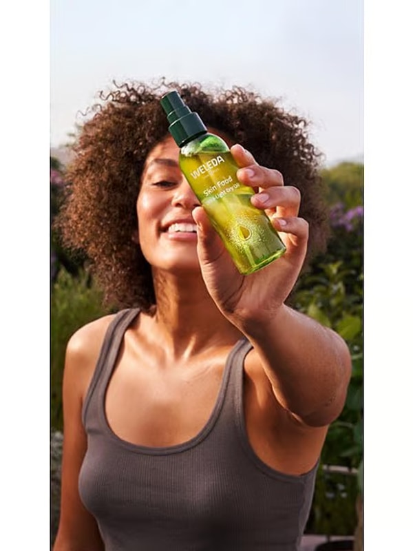 Woman holding Weleda Skin Food Ultra-Light Dry Oil outdoors
