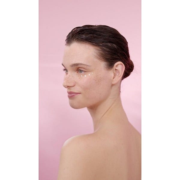 Woman's profile with Smoothing Wild Rose & White Tea cream on her face in a pink background.