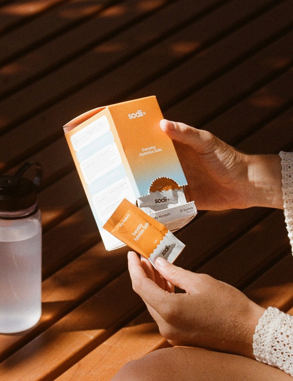 Sodii Everyday Hydration Salts Salty Mandarin box being opened beside a water bottle