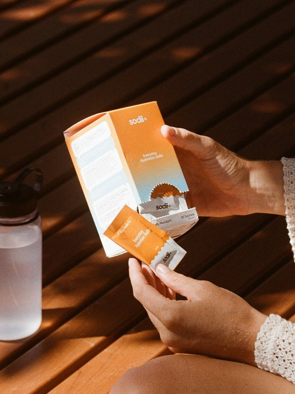 Sodii Everyday Hydration Salts Salty Mandarin box being opened beside a water bottle
