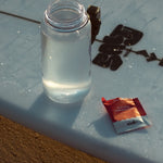Sodii Everyday Hydration Salts Salty Raspberry beside a water bottle in the sun