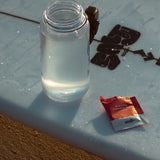 Sodii Everyday Hydration Salts Salty Raspberry beside a water bottle in the sun