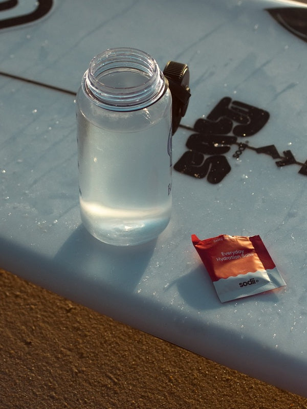 Sodii Everyday Hydration Salts Salty Raspberry beside a water bottle in the sun