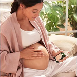 Pregnant woman applying Weleda Stretch Mark Massage Oil to her belly.