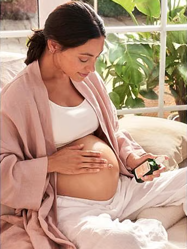 Pregnant woman applying Weleda Stretch Mark Massage Oil to her belly.