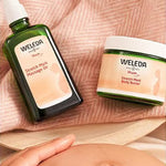 Weleda Stretch Mark Massage Oil and Body Butter beside a pregnant belly.