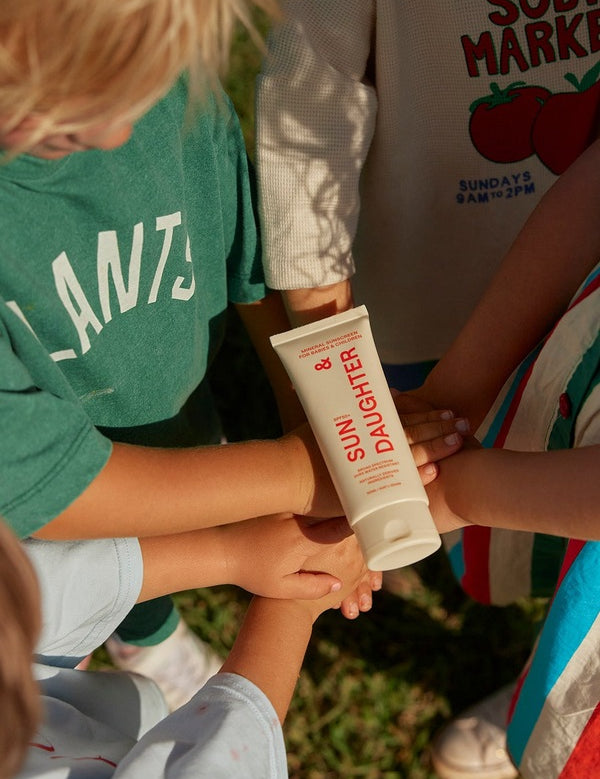 Children outdoors placing their hands together beneath a tube of Sun & Daughter SPF50 Mineral Sunscreen for Babies and Children.