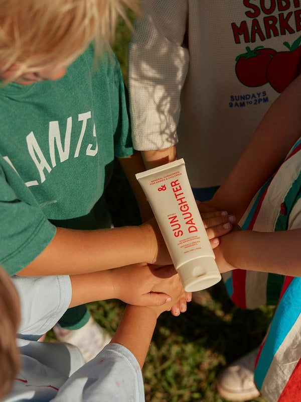 Children outdoors placing their hands together beneath a tube of Sun & Daughter SPF50 Mineral Sunscreen for Babies and Children.