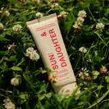 Ivory Sun & Daughter SPF50 Mineral Sunscreen for Babies & Children 100ml tube resting among green clover leaves and small white flowers in sunlight.