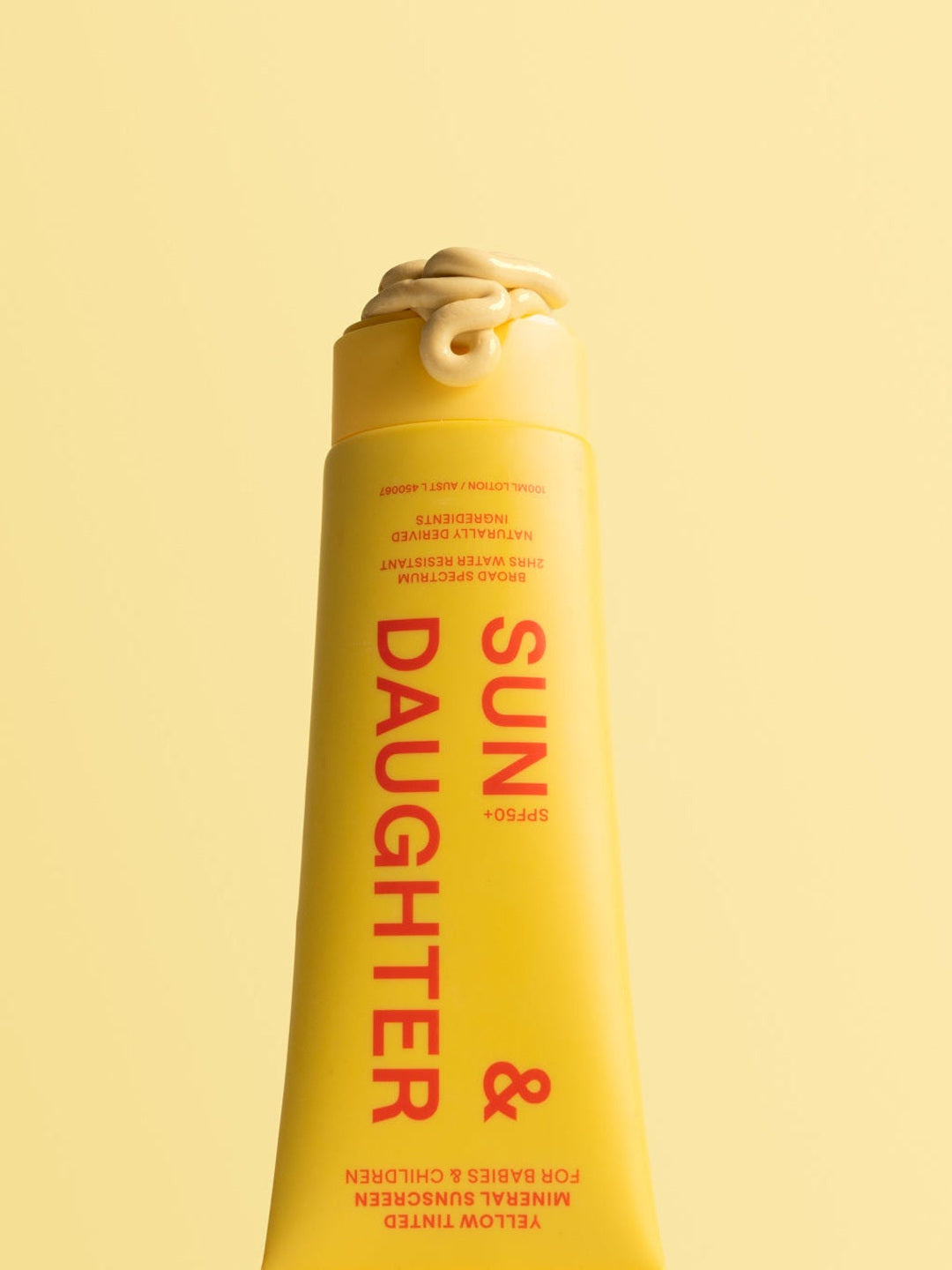Close-up of an uncapped yellow Sun & Daughter mineral sunscreen tube with a curl of pale yellow lotion at the opening, set against a yellow background.