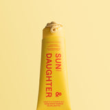 Close-up of an uncapped yellow Sun & Daughter mineral sunscreen tube with a curl of pale yellow lotion at the opening, set against a yellow background.