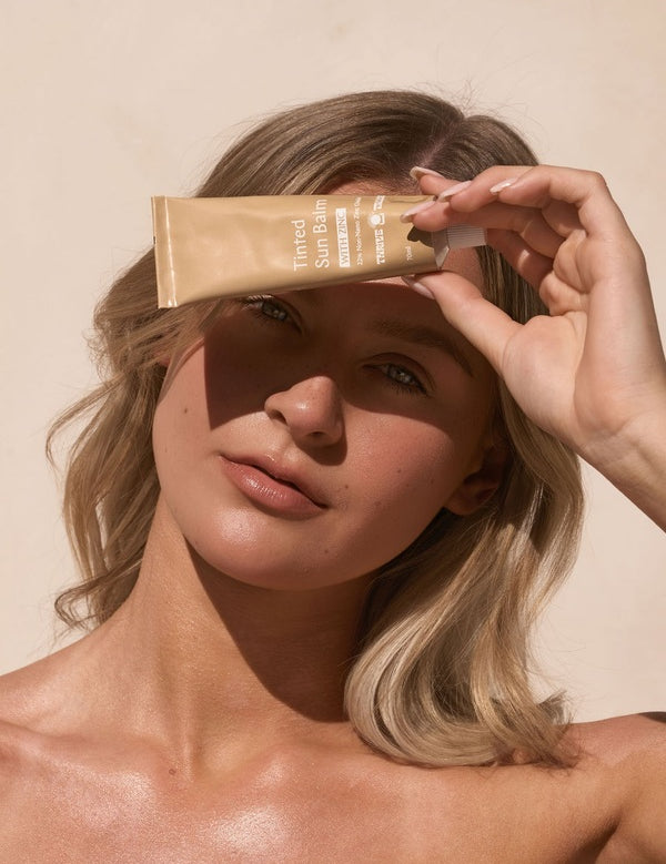 Woman holding Tinted Sun Balm in sunlight – Thrive Tallow Tinted Sun Balm with Zinc 70ml