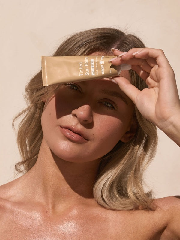 Woman holding Tinted Sun Balm in sunlight – Thrive Tallow Tinted Sun Balm with Zinc 70ml