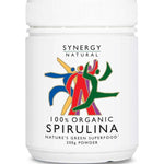 White Synergy Natural Organic Spirulina powder tub with a broad ribbed white lid and colourful red, green, blue and yellow figures above black 'SPIRULINA' lettering.