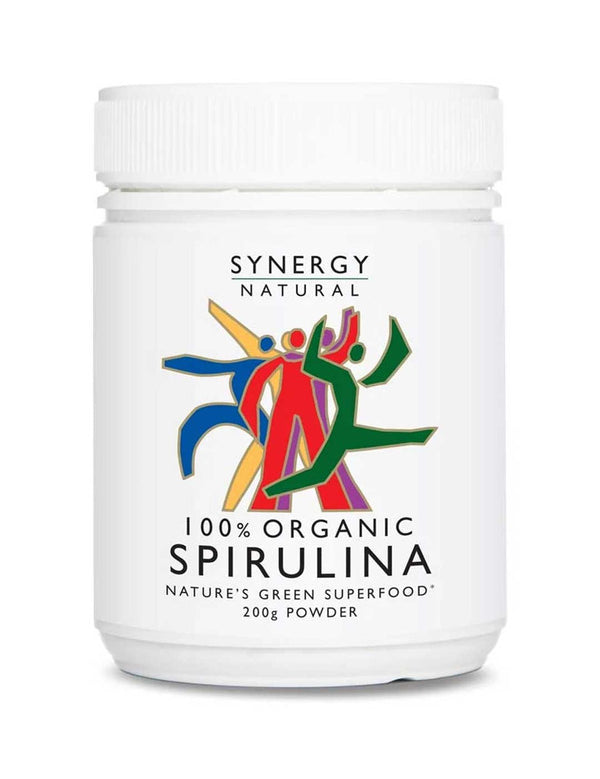 White Synergy Natural Organic Spirulina powder tub with a broad ribbed white lid and colourful red, green, blue and yellow figures above black 'SPIRULINA' lettering.