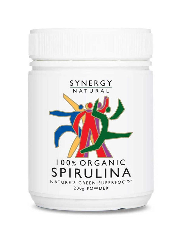 White Synergy Natural Organic Spirulina powder tub with a broad ribbed white lid and colourful red, green, blue and yellow figures above black 'SPIRULINA' lettering.