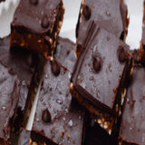 Close-up of chocolate energy bars made with The Beauty Chef Body Wellness Chocolate, sliced into squares and scattered with cacao nibs.