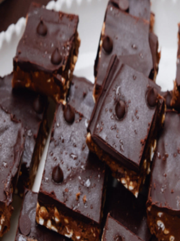 Close-up of chocolate energy bars made with The Beauty Chef Body Wellness Chocolate, sliced into squares and scattered with cacao nibs.