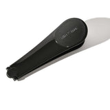 Black Three Warriors Self-Tan Back Applicator folded in half, with its tapered handles together and a rounded end casting a long shadow.