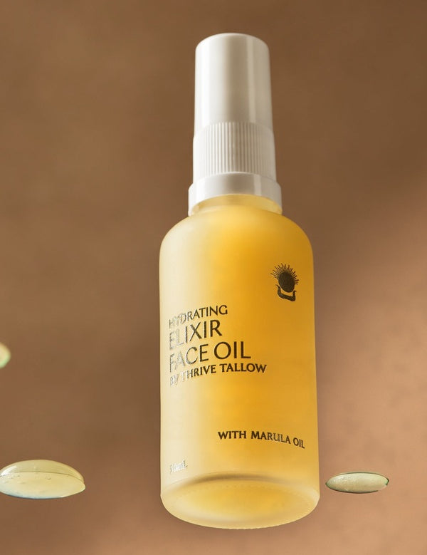 Golden Thrive Tallow Hydrating Elixir Face Oil 50ml bottle standing among glossy oil droplets in warm amber light.