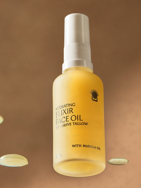 Golden Thrive Tallow Hydrating Elixir Face Oil 50ml bottle standing among glossy oil droplets in warm amber light.