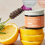 Thrive Tallow Scented Whipped Tallow Moisturiser jar styled with fresh lemon halves and lavender, with Clean and Conscious Awards badges above.