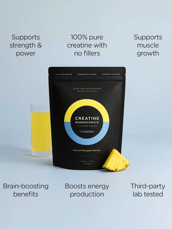 A black pouch of Tropeaka Creatine Monohydrate Pineapple 200g sits beside a glass of yellow pineapple drink and a pineapple slice, with text showing benefits such as muscle strength, energy, brain support, purity, and lab testing.