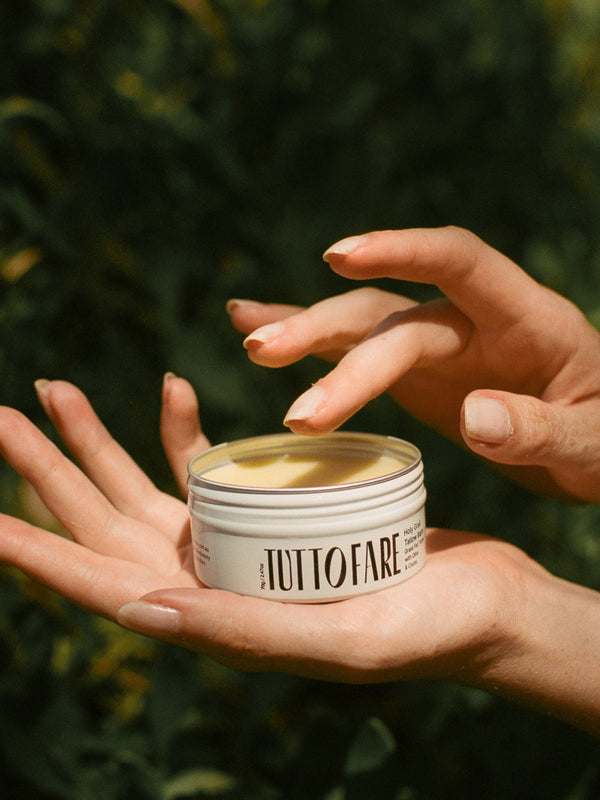 Hand holding an open tin of Tuttofare Holy Grail Tallow Balm
