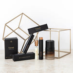 Formë perfume collection with slim black sprays, a pale refill vial and a larger dark amber bottle, arranged among black cartons and gold wire-frame cubes.