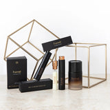 Formë perfume collection with slim black sprays, a pale refill vial and a larger dark amber bottle, arranged among black cartons and gold wire-frame cubes.