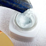 Blue stone spatula lifting Vanessa Megan AEON Azure Regenerative Cream from an open white jar on a textured white towel, with the gold lid partly visible.