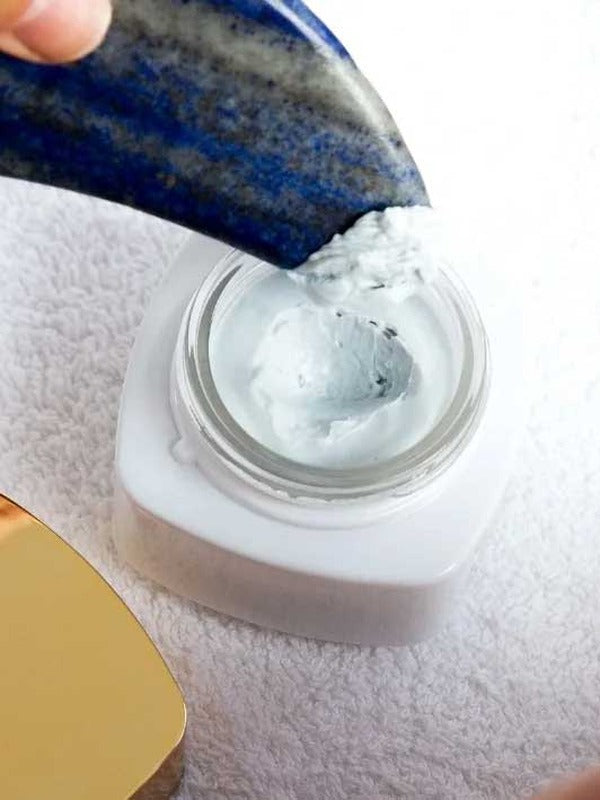 Blue stone spatula lifting Vanessa Megan AEON Azure Regenerative Cream from an open white jar on a textured white towel, with the gold lid partly visible.