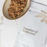 Vanessa Megan Rapadura and Wattleseed Body Buff pouch styled beside a wooden scoop filled with the textured body exfoliant and scattered wattleseed.
