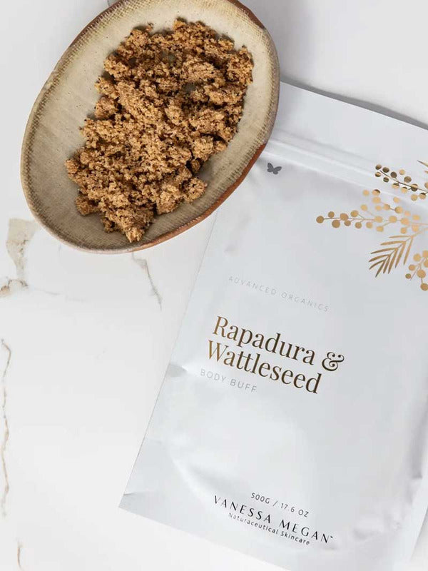 Vanessa Megan Rapadura and Wattleseed Body Buff pouch styled beside a wooden scoop filled with the textured body exfoliant and scattered wattleseed.
