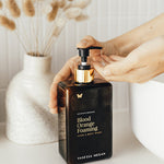 Hand reaching for Vanessa Megan Blood Orange and Vetiver Body Wash