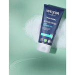 Tube of Weleda Men Active Fresh3-in-1 Shower Gel with eucalyptus and vetiver, surrounded by foam and gel on a light green background.