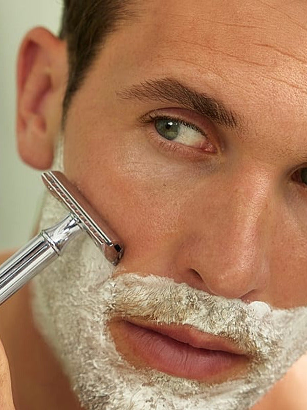 Man shaving in a mirror with Weleda For Men Shaving Cream lathered across his face.