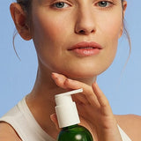 Young woman holding a bottle of Make-up Removal Cleansing Oil on a light blue background.