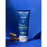 Weleda Men 2 in 1 Face Wash tube standing upright with pieces of liquorice root against a rich blue studio background.