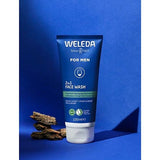 Weleda Men 2 in 1 Face Wash tube standing upright with pieces of liquorice root against a rich blue studio background.