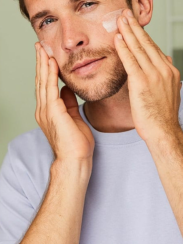 Man massaging Weleda Men 5 in 1 Multi-Action Serum into both cheeks during his skincare routine.
